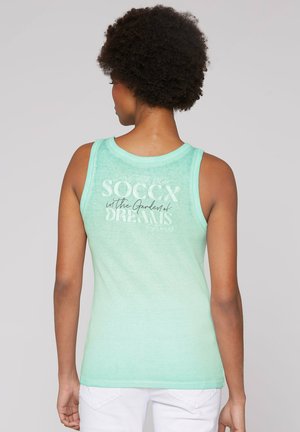 Mintgrünes Tanktop mit weichem Textil. Große weiße Schriftzüge auf dem Rücken mit der Aufschrift „Soccx im Garten der Träume“. Ärmelloses Design.