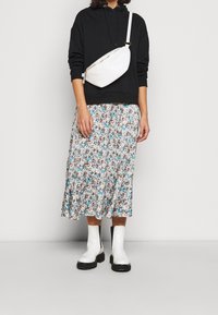 Svart hoodie, vit midikjol med blommönster och blå detaljer, vit axelväska och kraftiga vita stövlar med svarta sulor. Mjuka texturer.