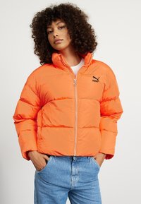 Giubbotto imbottito di colore arancione brillante, con colletto alto, chiusura a zip e un piccolo logo Puma nero. Design a coste e trapuntato.