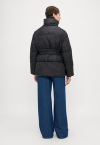 Čierna prešívaná bunda s vysokým golierom, opaskom v páse a prešívaným dizajnom. Skombinovaná s džínsami s širokými nohavicami pre ležérny vzhľad.