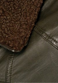 Brauner Lammfellkragen, der an einer dunklen Lederjacke befestigt ist, mit einem Reißverschluss und sichtbaren Nähten entlang der Nähte.