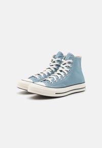 Wysokie trampki w jasnoniebieskim płótnie z białymi sznurowadłami, gumową podeszwą i kontrastującym czarnym wykończeniem. Charakteryzują się klasycznym, haftowanym wzorem.