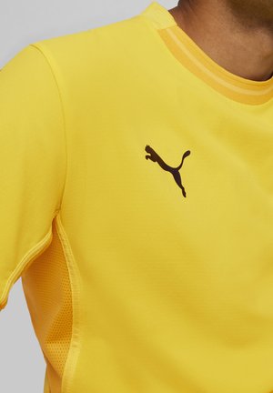 Maillot de sport jaune en tissu texturé, présentant un logo noir sur la poitrine et des détails en mesh sur les côtés pour la respirabilité.