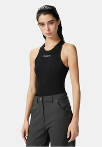 Body nero a coste con scollatura alta e logo sul davanti, abbinato a pantaloni grigi su misura con tasche laterali e chiusura con bottone.