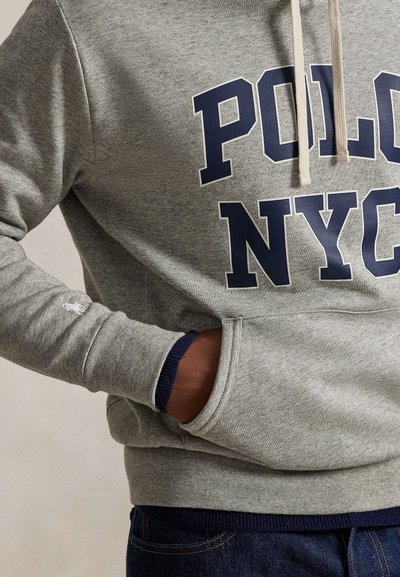 Γκρίζο φούτερ με κουκούλα, με τη φράση "POLO NYC" σε μπλε σκούρα γράμματα, κορδόνια, μπροστινή τσέπη και ριμπ μανσέτες σε μπλε σκούρο χρώμα, κατασκευασμένο από απαλό ύφασμα μείγματος βαμβακιού.