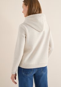 Hoodie gris clair avec une coupe décontractée, des poignets côtelés et une poche kangourou. Associé à un jean en denim bleu, vu de dos.