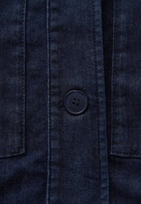 Chemise en jean foncé avec une fermeture à boutons classique. Les détails notables incluent deux poches poitrine et un tissu texturé avec des coutures subtiles.