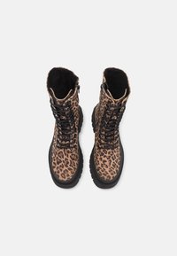 Paire de bottes de combat à lacets imprimées léopard avec semelles noires sur fond blanc, vue de dessus.