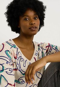 Pull en tricot beige avec des motifs de lignes abstraits colorés en bleu, vert et rouge, avec un col en V et des détails fins.