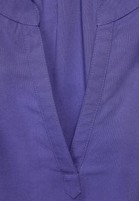 Top a V nel tessuto viola intenso con una texture morbida e cuciture a contrasto lungo il colletto e la patta.