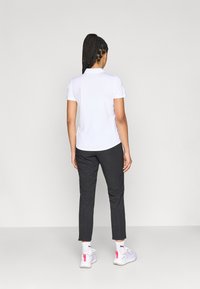 Λευκή κοντομάνικη μπλούζα πόλο συνδυασμένη με σκούρο παντελόνι. Το ντύσιμο διαθέτει άνετη εφαρμογή και κλασικό γιακά.