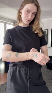 Black short-sleeve t-shirt and black drawstring pants worn by a person with visible tattoos. Gold hoop earrings add a metallic accent.