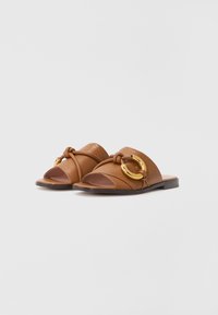 Brune lær slide sandaler med en knyttet rem og en gull sirkulær aksent. Åpen tå-design med en flat tre såle.