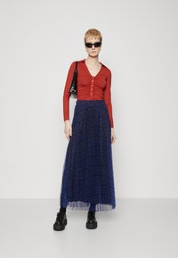 Tricou roșu cu mânecă lungă și detalii cu nasturi, combinat cu o fustă maxi albastră fluidă, cu un model de dungi de tigru, și pantofi platform negri, masivi.