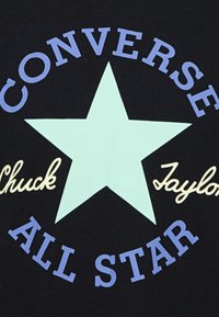 Tela negra con una gran estrella verde claro, con "CONVERSE" en morado arriba y "Chuck Taylor ALL STAR" en crema y morado debajo de la estrella.