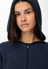 Marineblauer Fleece-Hoodie mit Reißverschluss vorne, ausgestattet mit einer weichen Textur und einer Kapuze. Reißverschluss und aufgerautes Innenfutter für Wärme.