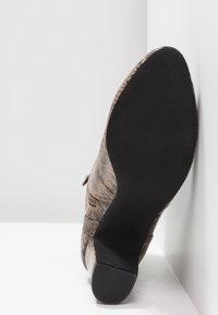 Brown texturized shoe profile, featuring a pointed toe and smooth black sole. Side appears with subtle stitching and a decorative accent.