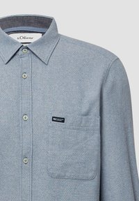Camicetta azzurro chiaro con un motivo testurizzato, colletto a punta e taschino sul petto con un'etichetta del marchio. Realizzata in tessuto intrecciato.