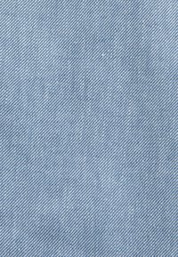 Ljust blå denimtyg med en diagonal twill-väv, som har en slät textur och subtila variationer i färg och nyans.
