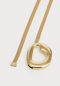 Collier pendentif en or avec une ouverture en forme de cœur, présentant une chaîne en or texturée et un petit fermoir carré. Détail logo gravé inclus.