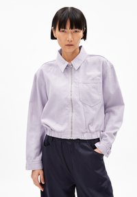 Chaqueta de mezclilla lavanda cortada, con cuello, cierre frontal y un bolsillo en el pecho. Cintura elástica y mangas largas. Textura suave.