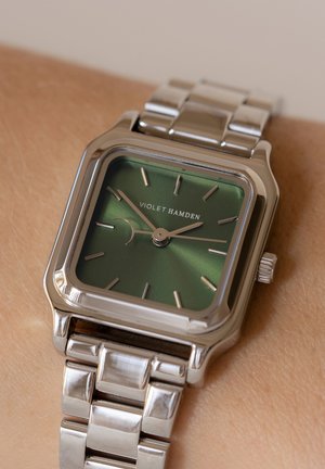 Square stainless steel watch with a green sunburst dial, silver hour markers, and a polished metal bracelet. Branding: "Violet Hamden."