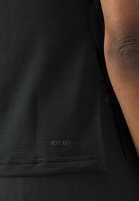 Schwarzes Sportoberteil mit geripptem Textur, "HEAT.RDY"-Logo und schlankem Design, mit einer Nahaufnahme des Saums und des Armbereichs.