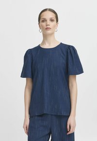 Marineblauwe top met korte mouwen en een ontspannen pasvorm, met een textuurstof die subtiele verticale strepen en pofmouwen heeft.