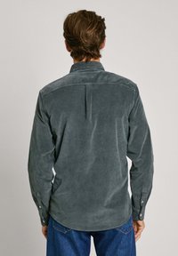 Camicia in corda grigia con polsini abbottonati e piega sul retro, caratterizzata da una texture morbida e orlo curvo, abbinata a jeans blu.