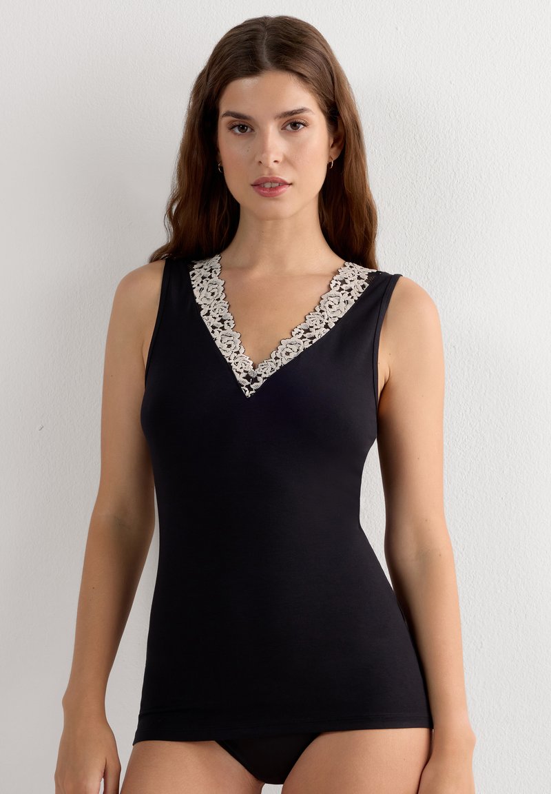 Jeune femme aux longs cheveux bruns portant un haut noir sans manches avec une bordure en dentelle blanche au col en V.