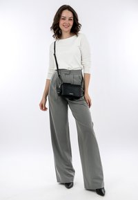 Weißes Langarmoberteil, hoch taillierte graue weite Hose und eine kleine schwarze Umhängetasche. Spitz zulaufende schwarze Absätze runden das Outfit ab.