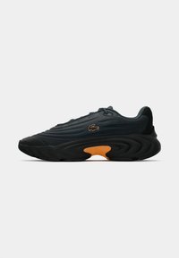 Sort og mørkegrå sports sneakers med orange sål-akkent og præget krokodillologo på siden, vist i profil på hvid baggrund.