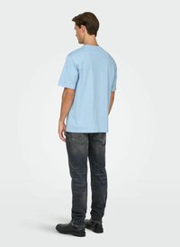 Light blue cotton T-shirt with a crew neckline, short sleeves, and a relaxed fit, paired with dark denim jeans and black shoes.