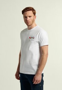 Camiseta de algodón blanca con cuello redondo, mangas cortas y detalles de estampado náutico colorido en el lado izquierdo del pecho.