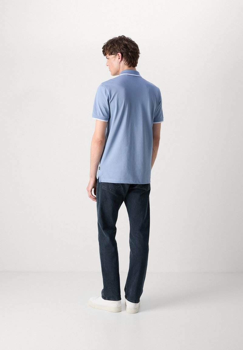 Polo shirt bleu clair avec un col classique et des manches courtes, associé à un jean foncé et des baskets blanches. Design épuré et minimal.