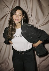 Černá denimová bunda se stříbrnými ozdobami na ramenou, bílý tričko s nápisem "LOVE", černé džíny a černý opasek.