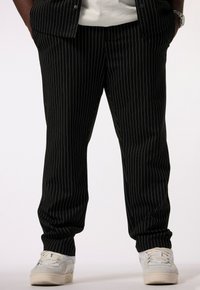 Pantalones de rayas negras con corte entallado, que presentan una textura suave. Combinados con zapatillas blancas para crear contraste. Cintura de altura media.