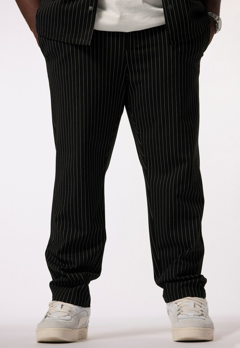 Pantalones de rayas negras con corte entallado, que presentan una textura suave. Combinados con zapatillas blancas para crear contraste. Cintura de altura media.