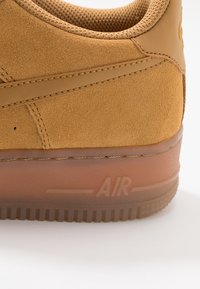 Zapatillas de ante en color beige con un acabado texturizado, que cuentan con una suela de goma y el logo "AIR" en relieve en el talón. Forma redondeada con un cuello acolchado.