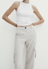 Witte geribbelde tanktop gecombineerd met lichtgrijze cargobroek met klepzakken en een knoopsluiting bij de taille.