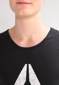 Black cotton T-shirt featuring a round neckline and a large, abstract gray graphic on the front. Smooth texture and casual design.