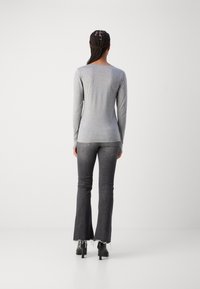 Graues Langarmshirt mit rundem Halsausschnitt, kombiniert mit dunkelgrauen Schlagjeans mit ausgefransten Säumen und schwarzen Absatzstiefeln.