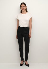 Maglietta bianca a maniche corte abbinata a jeans skinny neri. I jeans presentano una chiusura con bottone e zip frontale, con tasche sottili e una texture liscia.