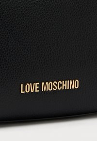 Μαύρη τσάντα χειρός από δερματίνη με υφή, με το χρυσό λογότυπο "LOVE MOSCHINO" να προβάλλεται έντονα. Διαθέτει λείο φινίρισμα και καθαρές γραμμές.
