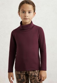 Bordeaux värvi pikakä sleeves turtleneck särk, millel on sile tekstuur, keritud krae ja kitsas lõige. Kantud mustriliste pruuni värvi pükstega.