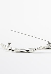 Zilverkleurige metalen naaigarenhouder met een gedraaide ontwerp, voorzien van een kleine sluiting en een verlengde naald. Gladde textuur en glanzende afwerking.