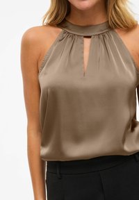 Silkblandede halterneck-top i beige med nøglehul foran, samlet halsudskæring og glat tekstur, parret med sorte tætsiddende bukser.