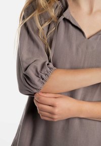 Losse, lichtgrijze blouse met een V-hals, pofmouwen en een gestructureerde stof. Heeft gathered details bij de mouwen.