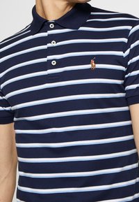 Polo tričko s námořnickou a světle modrou pruhovanou kombinací, vyrobené z bavlny, s klasickým límcem, zapínáním na tři knoflíky a malým vyšitým logem.