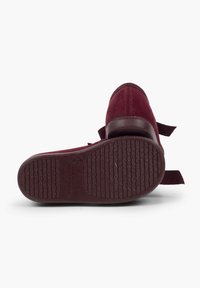 Scarpe in suede bordeaux con suola in gomma texturizzata, tacco piatto e linguetta in tessuto sul retro per una facile calzata. Cuciture visibili che accentuano le cuciture.